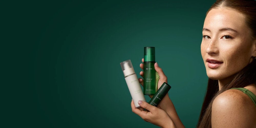 A woman holding THREE Visage Radiant Toner, Pure Cleanse and Super Serum against a green backdrop