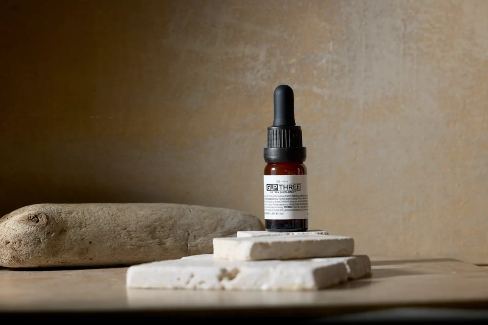 A bottle of GLP THREE drops standing on white stone tiles