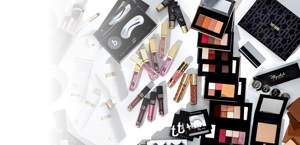 A flat lay of Tori Belle lip glosses, eyeshadow palettes, brow kits, skincare tubes and boxed magnetic lashes on a white surface