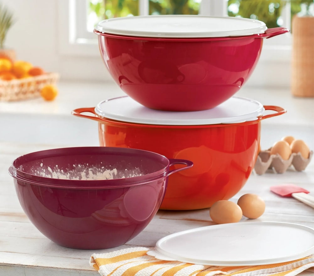 Three Thatsa Bowls in red, orange and plum on a kitchen counter with eggs, flour and a striped towel