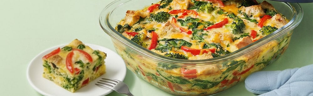Vegetable strata baked in a Tupperware glass dish with a slice served on a plate