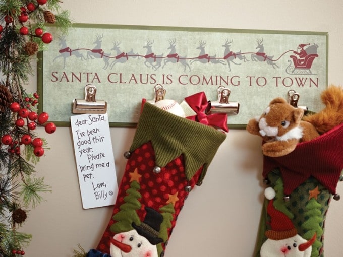 Christmas stockings hanging from a wall board lettered Santa Claus Is Coming to Town, next to a child's letter to Santa