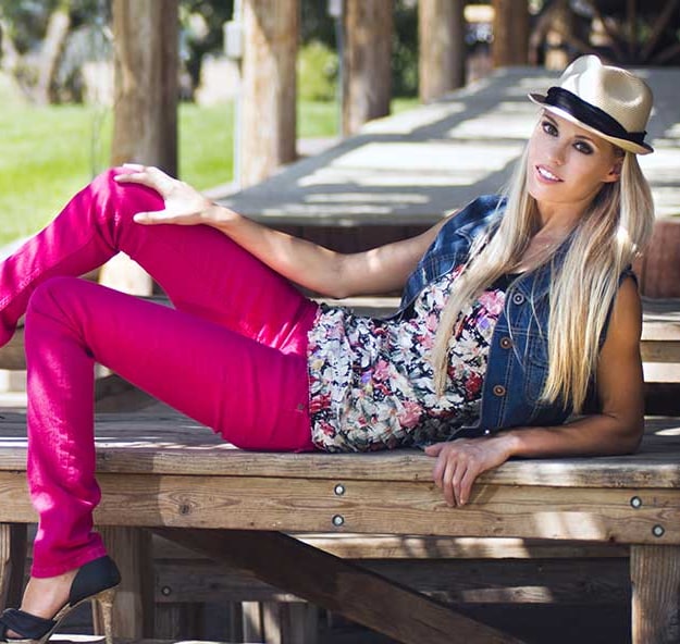 A woman in pink jeans and a denim vest reclining on a wooden picnic table in the sun