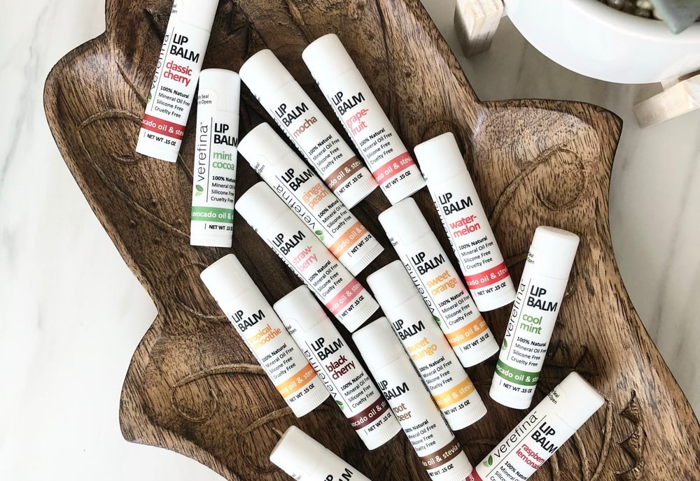 A carved wooden dish piled with Verefina lip balms in assorted flavors