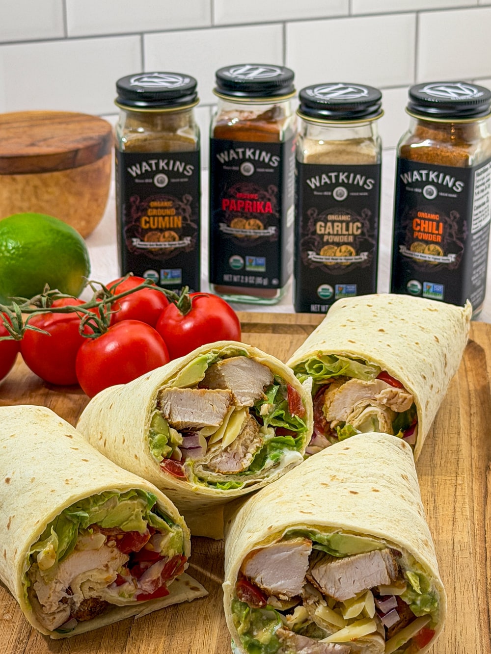 Chicken avocado wraps on a cutting board in front of jars of Watkins organic cumin, paprika, garlic powder and chili powder