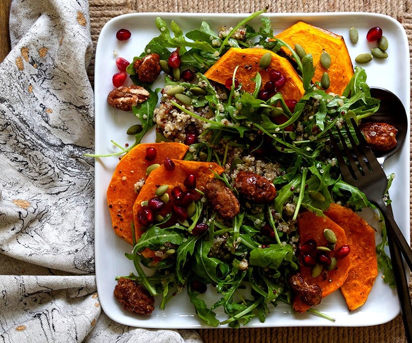 A roasted butternut squash, quinoa and arugula salad with pomegranate seeds and candied pecans on a white platter