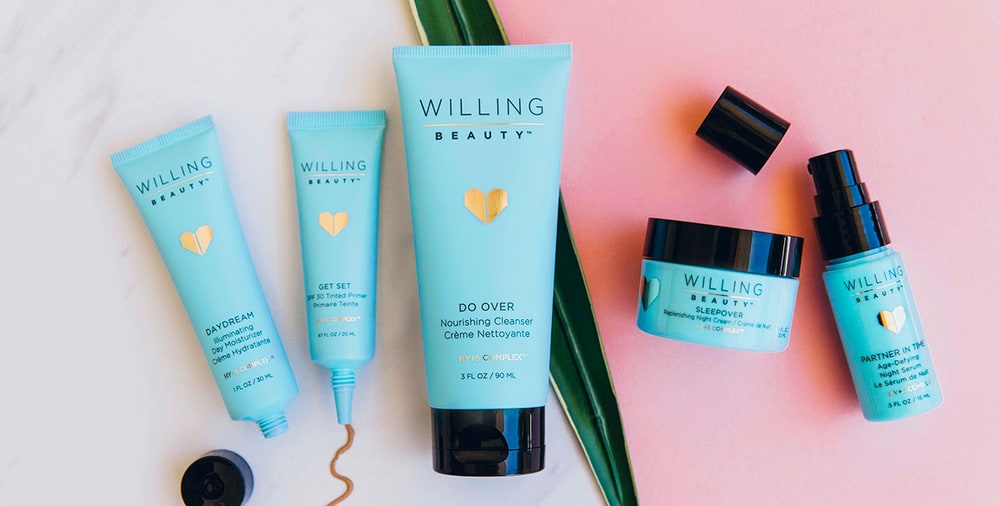 Turquoise Willing Beauty tubes and jars, including Daydream moisturizer, Get Set primer, Do Over cleanser, Sleepover night cream and Partner in Time serum, on marble and pink
