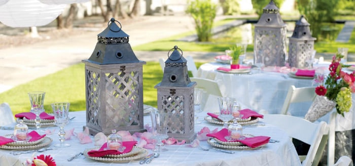 Grey lattice lanterns, pink napkins and beaded-rim plates set on white-clothed tables at an outdoor garden party