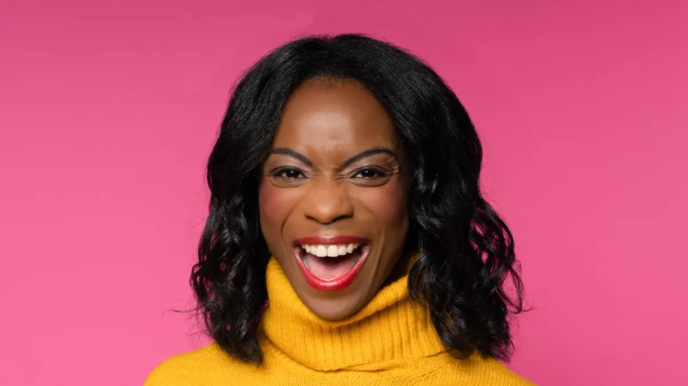 Smiling woman in a yellow sweater wearing red Younique lip color against a pink background