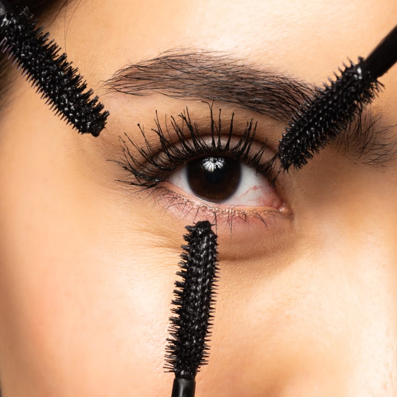 Close-up of an eye with three Younique mascara wands held around the lashes