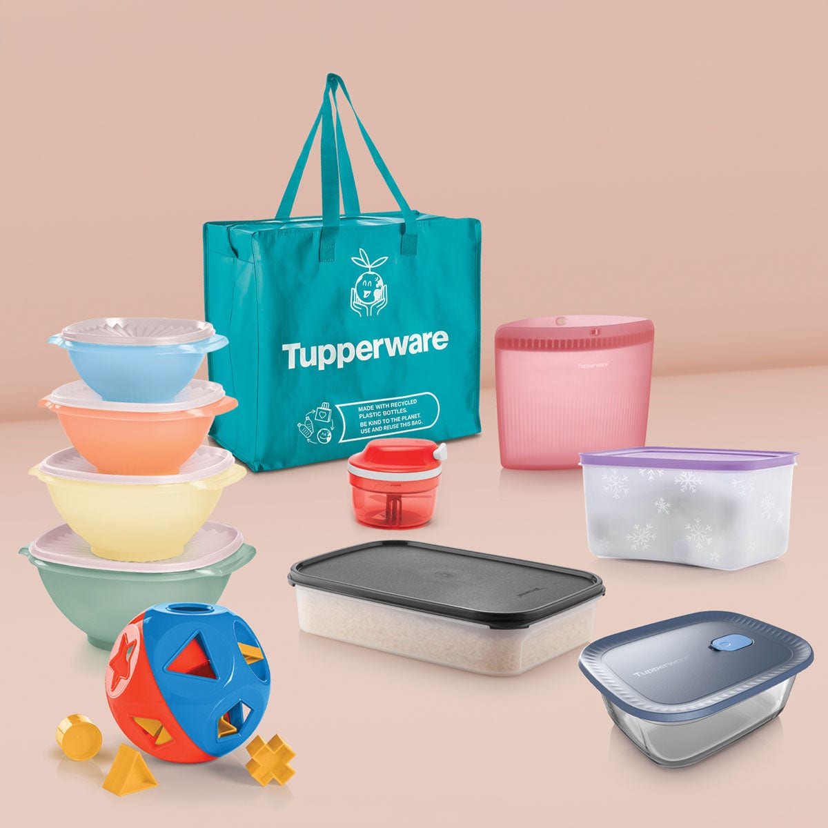 The Tupperware Deluxe Business Kit: a teal tote bag, four stacked Servalier bowls, a Shape-O toy, a red SuperSonic chopper, a pink silicone bag, a Freezer Mates container, a Modular Mates container and a Voila glass dish