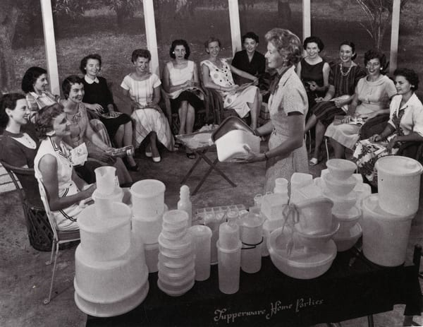 A black-and-white 1958 photograph of a woman demonstrating a Tupperware bowl to a circle of seated women at a home party in Sarasota, Florida